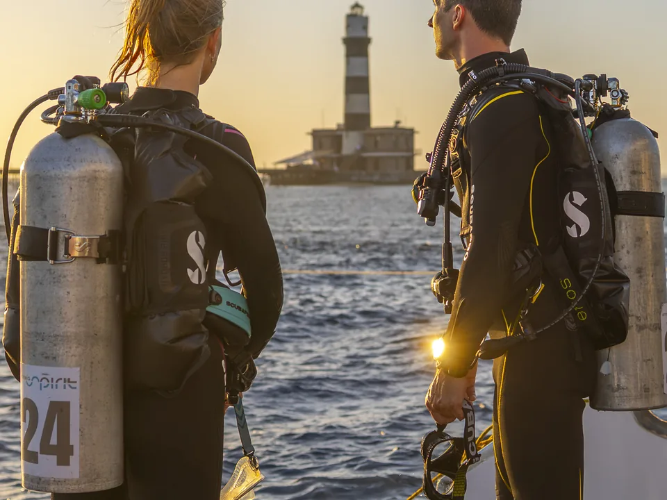 Zwei Taucher mit deutlich sichtbaren Tauchflaschen am Wasser